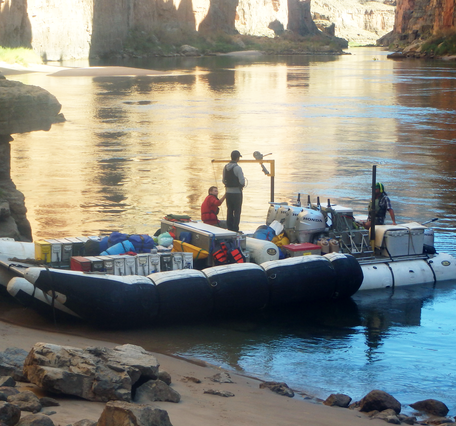 Researchers stand on a boat that's parked on a sandbar along the Colorado River in Grand Canyon