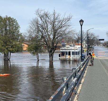 Hydrologic technician takes acoustic Doppler current profiler measurement of flooded river from bridge