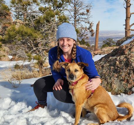 photo of a woman in snow wearing blue hat with dog