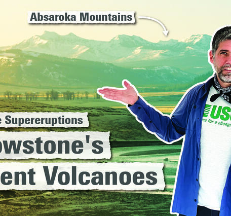 Man in blue shirt points to rugged snow-capped mountains in the background