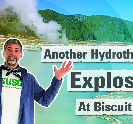 Man in blue shirt holding hands up with a blue pool and spouting geyser in the background