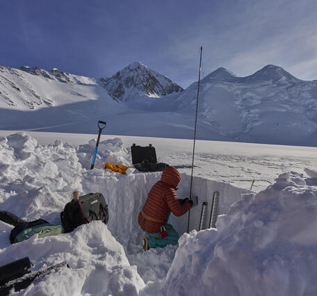 Person in a red jacket kneeling in a pit in the snow.