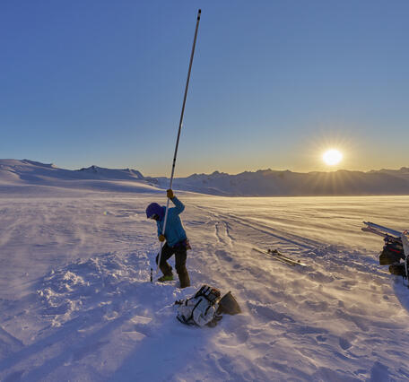 Person holding a lake stake vertically on a glacier.