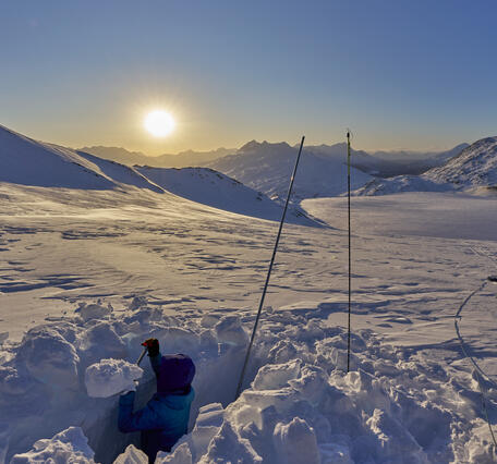 Snow pit on glacier with sun setting in background.