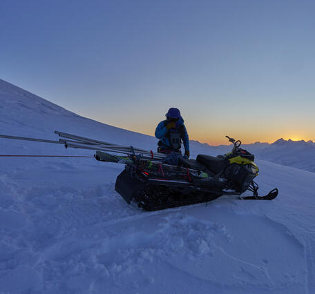 Person standing near a snowmachine on a glacier.
