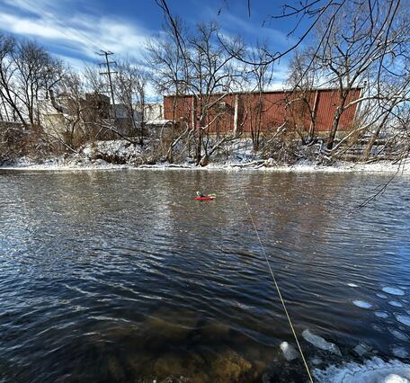 acoustic Doppler current profiler floats in middle of river attached to cable across on a winter day