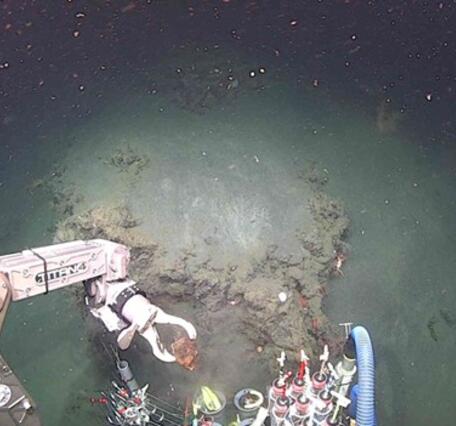 An underwater view from the submersible Alvin showing the manipulator arm picking up a rock from the seafloor