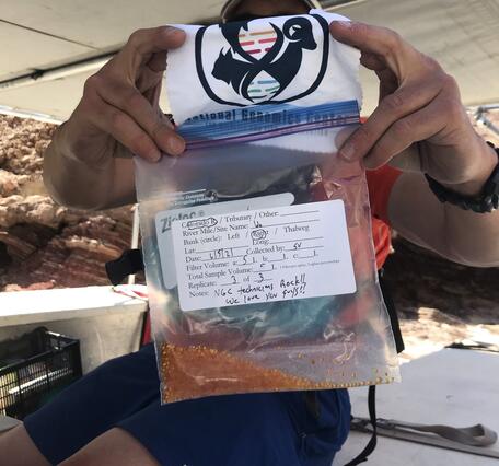A close-up of a technician's hands holding an eDNA sample in a labeled biohazard plastic bag