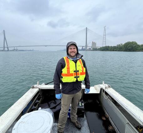 Man standing on boat with large bridge in background