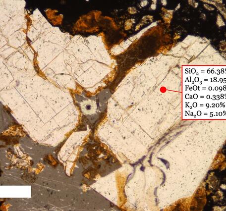 Microscope view of beige irregular and broken crystal surrounded by gray material. Chemical composition given for one point.