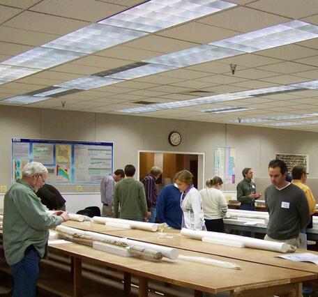 A room of people examine rock core laid out on a table