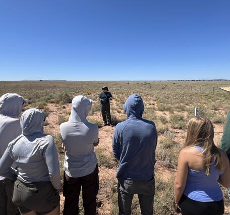 Students watch a USGS ecologist describe restoration experiments in a field in Northern Arizona rangelands