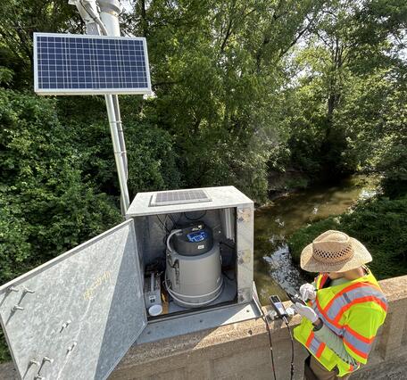 Scientist collecting field parameters and checking the autosampler at streamgage on bridge