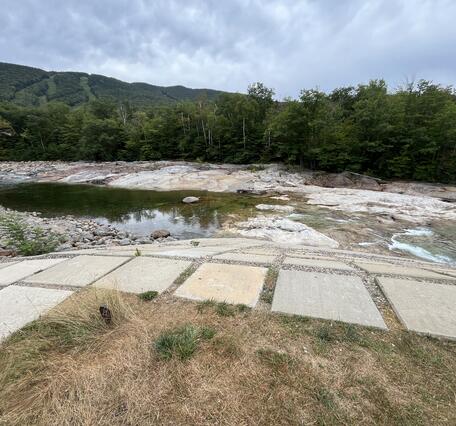 Low lying water in a river with a ski resort in the background during the summer.