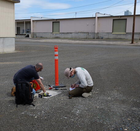 Scientists measure well in a gravel lot