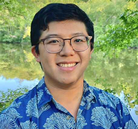 Color photograph of male with aloha shirt on and greenery in the background