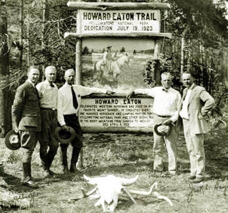Five men in 1920s-era suits stand in front of a wooden sign for Howard Eaton Trail; forest behind and bison skull in front