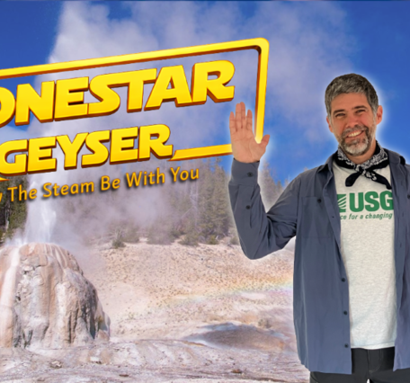 Many with arms raised standing in front of am erupting geyser with forest and blue sky in the background
