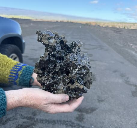 Color photograph of scientist holding a sample of lava