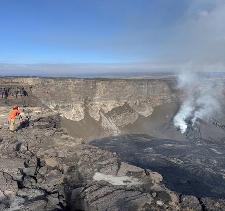 Color photograph of volcanic crater with geologist on rim