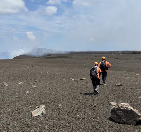 Color photograph of two scientists walking on volcanic landscape