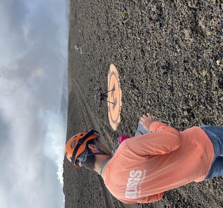 Color photograph of scientist operating UAS on volcanic terrain