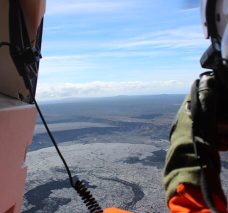 Color photograph of scientist taking photos from helicopter