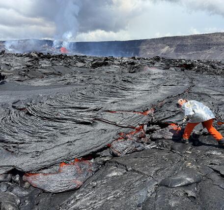 Scientist uses a hammer to collect a red molten lava sample from a lava flow.