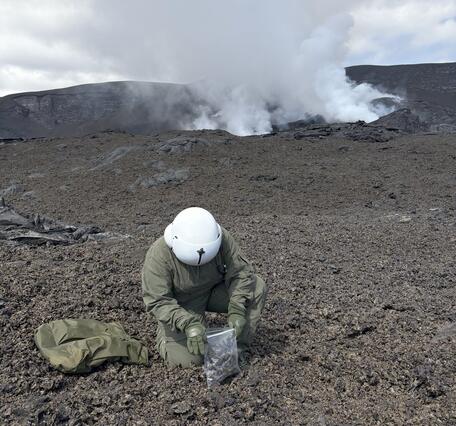 Color photograph of scientist collecting geologic samples near degassing volcanic vent