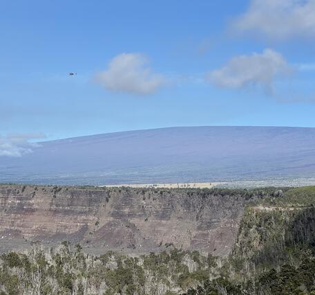 Color photograph of shield volcano with caldera wall in the foreground