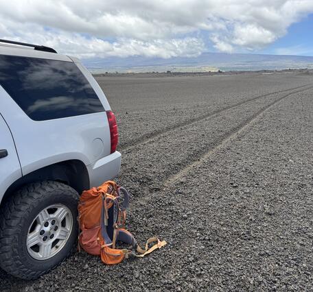 Color photograph of vehicle on volcanic terrain with tire tracks in the background