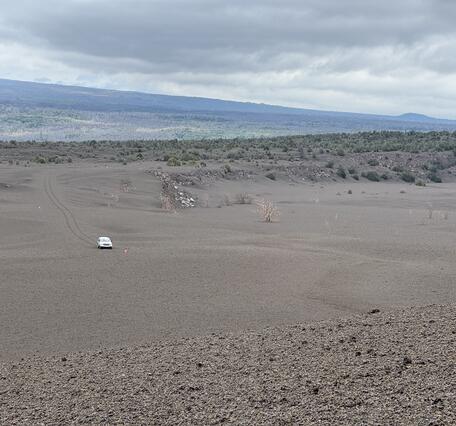 Color photograph of volcanic landscape with car driving in the distance