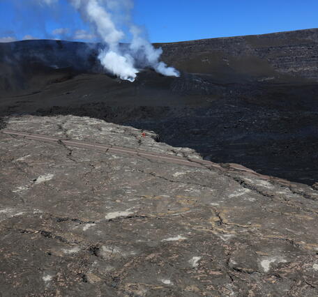 color photo of a scientists working on a field site from a distance with the vents in the background. 