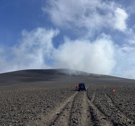 Color photograph of volcanic hill with road and vehicle in the foreground
