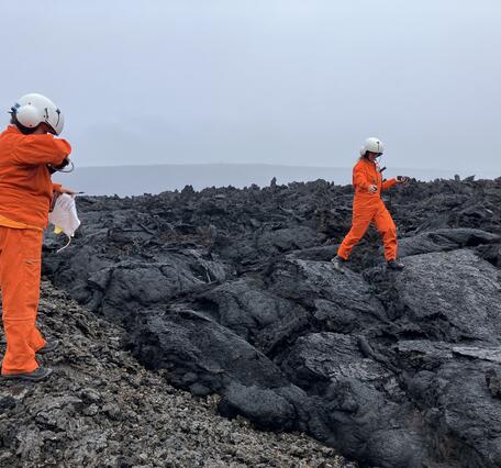 Color photograph of two scientists collecting samples from cooled lava flows