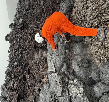 Color photograph of scientist collecting sample of cooled lava flow