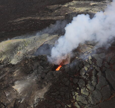 Color photograph of volcanic vent with roiling lava in it