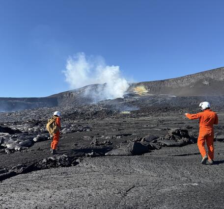 Color photograph of scientists in orange flight suits on a volcanic landscape