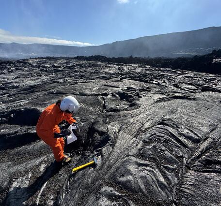Color photograph of scientist collecting sample of cooled and solidified lava from a recent eruption 