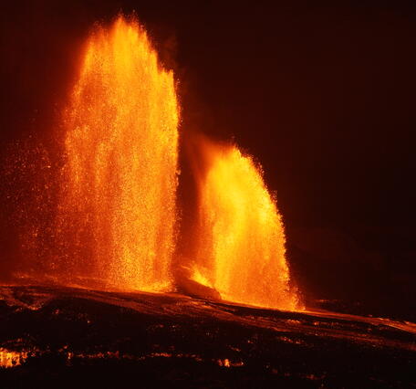 Color photograph of two lava fountains at night