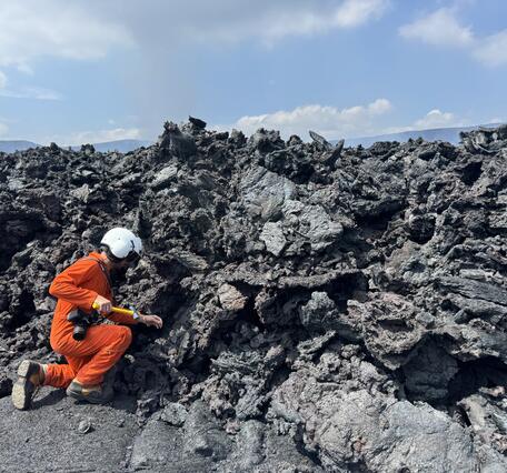 Color photograph of scientist collecting sample of lava flow
