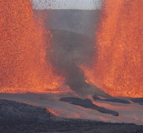 Color photograph of the base of two lava fountains and lava flowing away from them