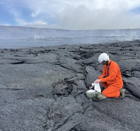 Color photograph of scientist collecting a sample from a recent lava flow