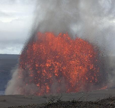 Color photograph of lava fountain with overcast skies in the background