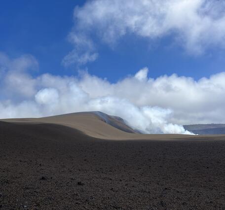 Color photograph of volcanic landscape with volcanic plume and clouds