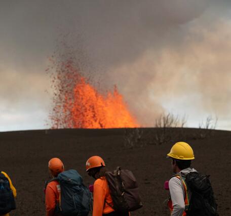 Color photograph of scientists with top of lava fountain in distance