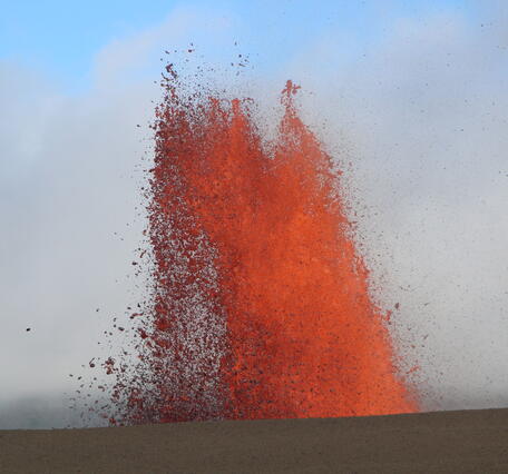 Color photograph of lava fountain visible above crater rim