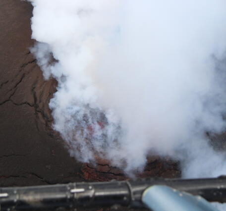 Color photograph of volcanic vent degassing with lava below