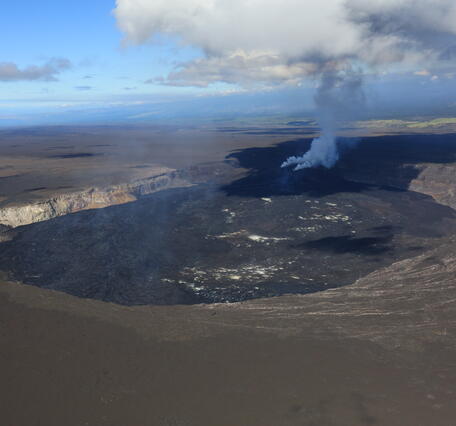 Color photograph of crater at summit of volcano with degassing plume from active vents