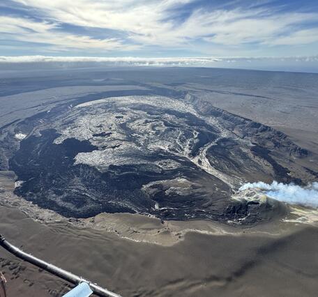 Color photograph of caldera at summit of volcano with gas plume from eruptive vents